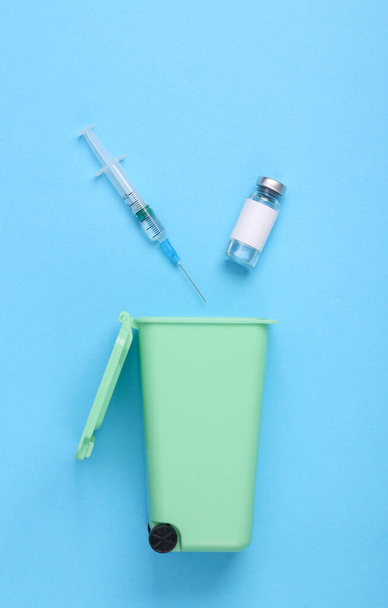 Бутылка вакцины со шприцем и мусорным баком на синем фоне - Фото, изображение