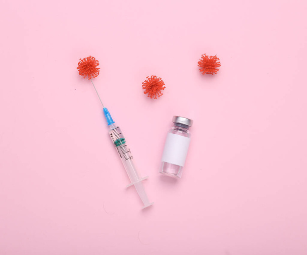 Εμβολιασμός, θεραπεία με covid 19. Φιάλη εμβολίου με κενή ετικέτα για το εμπορικό σήμα, μόρια ιών και σύριγγα σε ροζ φόντο. Στο πάνω μέρος. Επίπεδη - Φωτογραφία, εικόνα