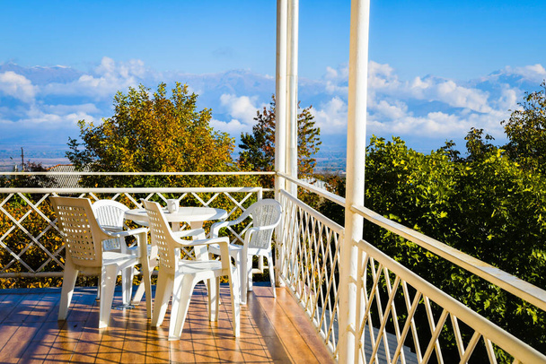 set of white chairs with table in traditional georgian balcony in city Telavi with beautiful mountains and alazani valley background to enjoy vacation in Caucasus - Photo, Image
