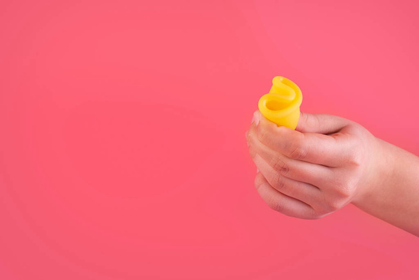 Vista de cerca de la mujer sosteniendo copa menstrual amarilla aislada sobre fondo rosa, período de la mujer, copa menstrual en las manos, métodos modernos para los días criticos. Concepto de productos de ginecología e higiene - Foto, imagen