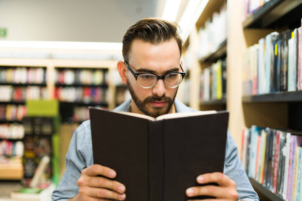 Fiksu kolmekymppinen mies lukee mielenkiintoista kirjaa ostaessaan kirjoja kirjakaupasta. - Valokuva, kuva