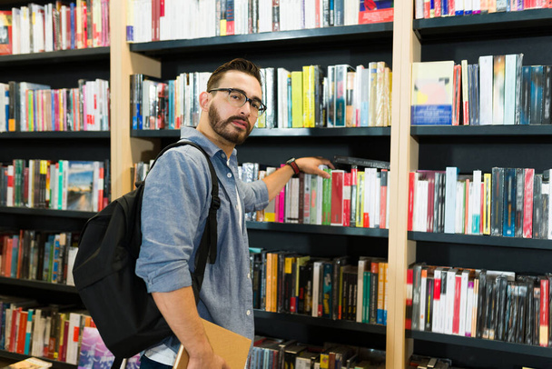 Продуманий читач чоловік з рюкзаком шукає роман на книжкових полицях книгарні
 - Фото, зображення