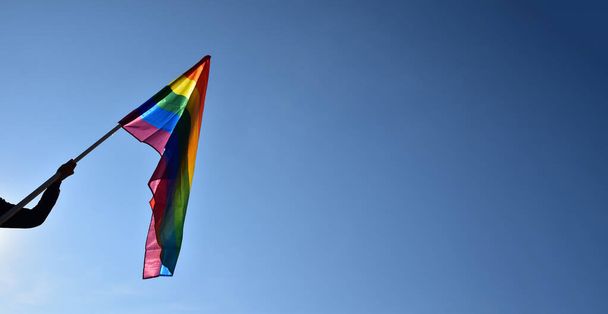 Рейнбоу-флаг, силуэт ЛГБТ, держащий в руках мальчика на ясном голубом фоне, мягкий и избирательный фокус, концепция празднования ЛГБТ в июне по всему миру, пространство для копирования. - Фото, изображение