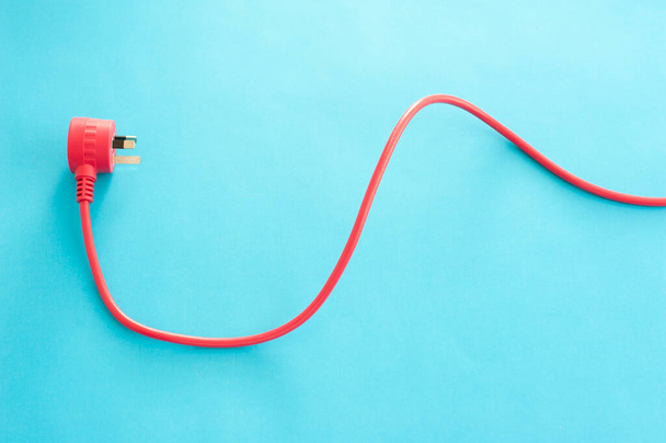 Red electric cord and integrated three prong earthed Australian plug in a wavy line on a blue background with copy space - Photo, Image