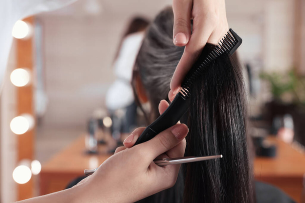 Professional hairdresser brushing woman's hair in beauty salon, closeup - Photo, Image