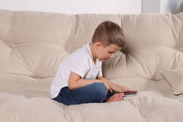 Boy with poor posture using phone on beige sofa indoors. Symptom of scoliosis - Foto, Bild
