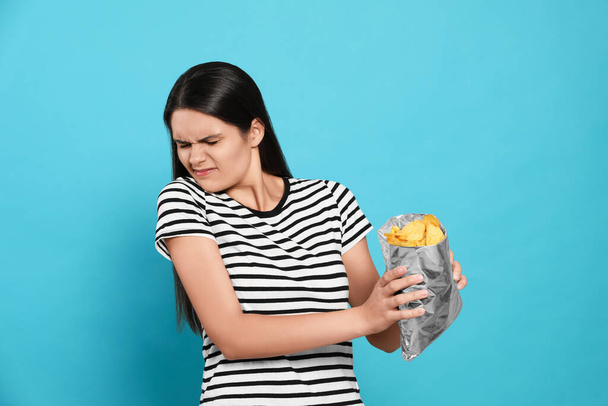 Beautiful woman refusing to eat potato chips on blue background - Fotoğraf, Görsel