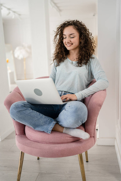 Eine junge erwachsene kaukasische Studentin, die am Laptop arbeitet, während sie in einem Stuhl sitzt, liest und tippt Online-Prüfung lernen zu Hause in hellen Raum Kopierraum echte Menschen Fernbildung - Foto, Bild