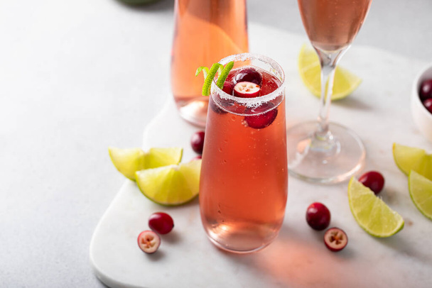 Christmas mimosa with cranberry juice and lime, garnished with lime twist, festive sparkling wine or rose cocktail idea - Fotoğraf, Görsel