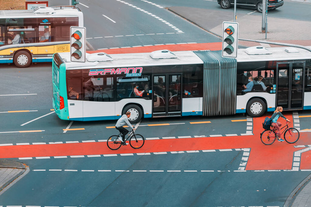 26 de julho de 2022, Munster, Alemanha: Um cruzamento urbano movimentado com ônibus de transporte público, carros e ciclistas andando em ciclovias. Tráfego de passageiros e prevenção de engarrafamentos - Foto, Imagem