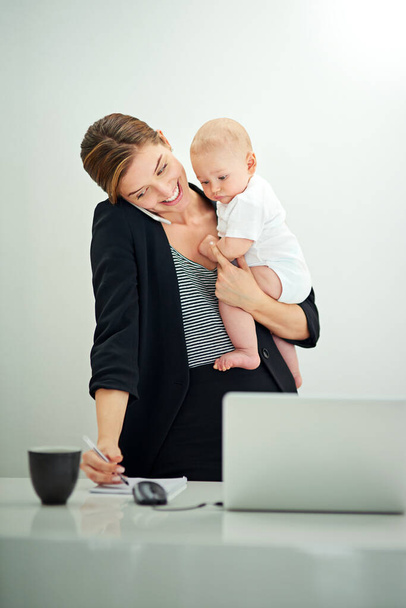 Building a business empire for her family. a successful young businesswoman carrying her adorable baby boy while talking on the phone - Valokuva, kuva