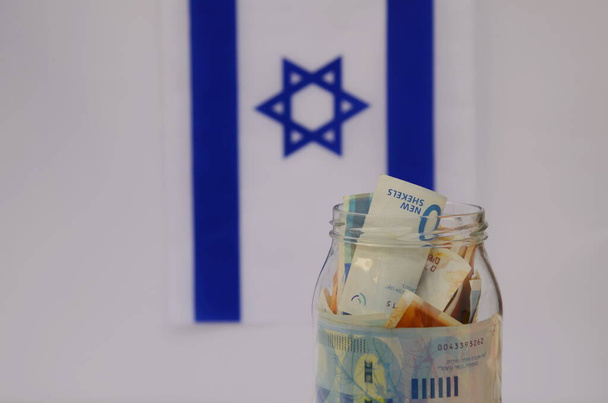 Üvegedény izraeli sékellel Izrael zászlajának hátterében. Koncepció: személyes megtakarítások, bankrendszer, infláció, nemzeti valuta - Fotó, kép