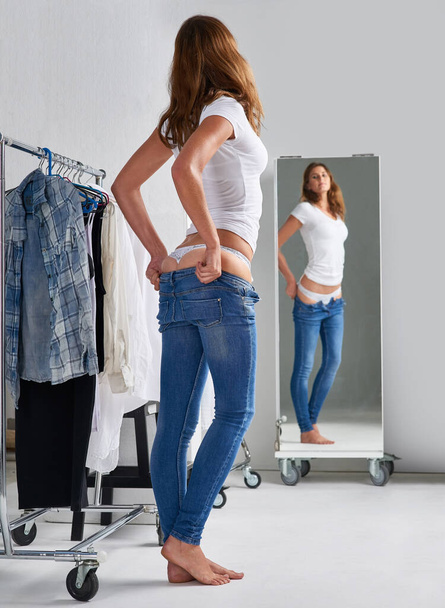 I like these already. an attractive young woman trying on jeans in a mirror - Photo, Image
