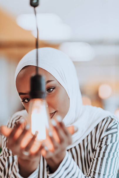 Sentimental portrait of African-American young female Muslim wearing hijab while holding a lightbulb - Fotografie, Obrázek