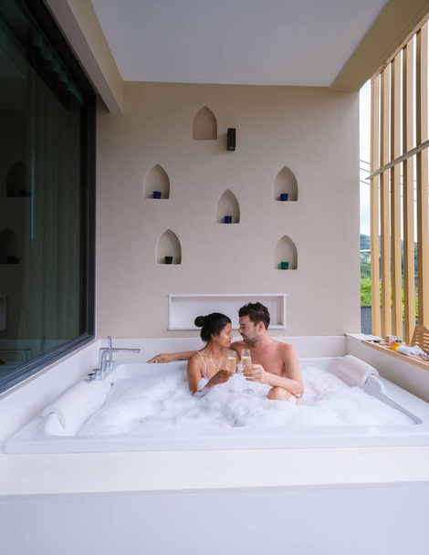 couple drinking champagne in a jacuzzi during honeymoon vacation, Asian Thai women and caucasian men in a bathtub jacuzzi - Photo, Image