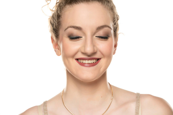 Mladá blonďatá usměvavá žena s kudrnatými vlasy a make-upem pózujícím na bílém pozadí. oči zavřené. - Fotografie, Obrázek