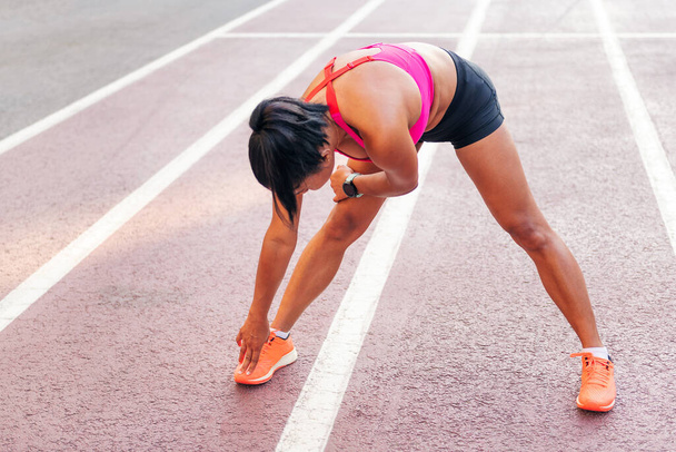 unrecognizable sportswoman stretching legs on the athletics track during her training, concept of urban sport and healthy lifestyle, copy space for text - Φωτογραφία, εικόνα
