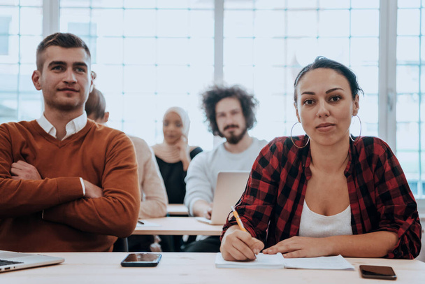 A group of diverse young men and women sit in a modern classroom and listen to a lecture on business training. High quality photo - Photo, Image