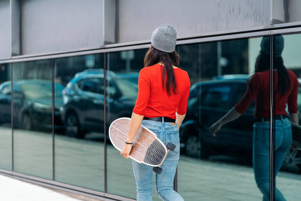 Unrecognized skater girl wearing hat walking in the street and holding her long-board. - Fotografie, Obrázek