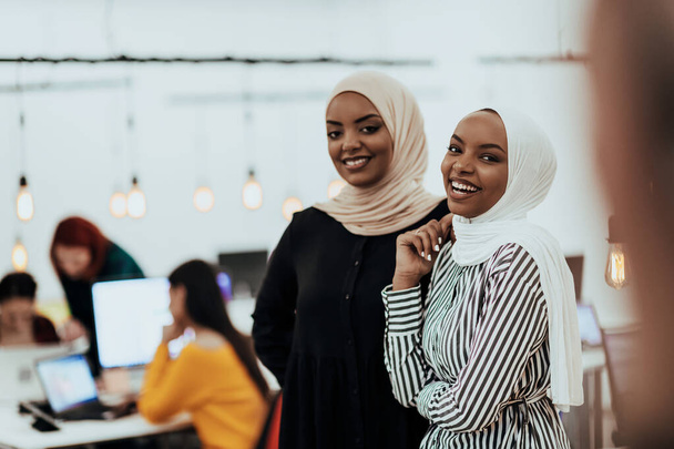 Portrait of two African American businesswomen talking to each other while standing in a modern business office with their colleagues. Marketing concept. Multi-ethnic society - Foto, imagen