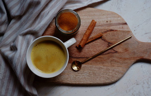 złote latte, filiżanka gorącej latte z paluszkami cynamonowymi na drewnianej desce do krojenia - Zdjęcie, obraz