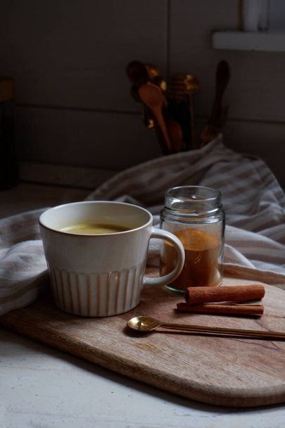 Altın latte, bir fincan sıcak zerdeçal latte ve tahtanın üzerinde tarçın çubukları. - Fotoğraf, Görsel