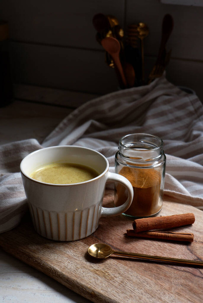 złote latte, filiżanka gorącej latte z paluszkami cynamonowymi na drewnianej desce do krojenia - Zdjęcie, obraz
