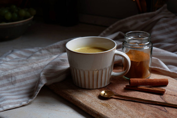golden latte, cup of hot turmeric latte with cinnamon sticks on wooden cutting board - 写真・画像