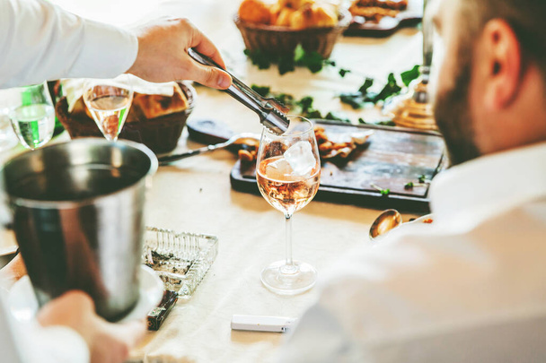 Θέα σε χέρια σερβιτόρου που σερβίρουν κρασί σε ποτήρια σε ξύλινο τραπέζι σε εστιατόριο. - Φωτογραφία, εικόνα