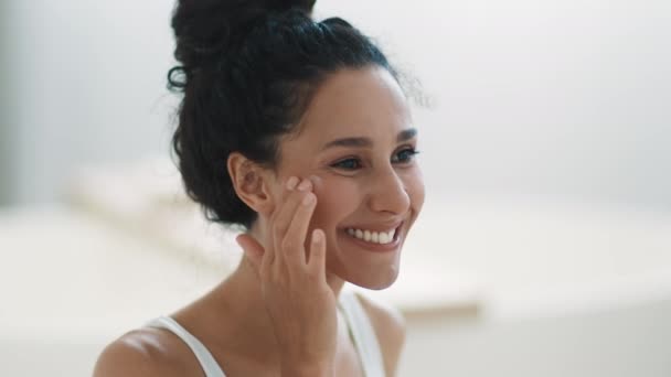 Youth and beauty care. Close up portrait of beautiful young woman applying moisturizing cream on her cheek, pampering face skin, looking aside, slow motion, empty space - Footage, Video