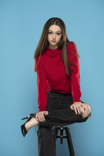Kırmızı bluzlu ve siyah kotlu hoş bir kız mavi stüdyo arka planında izole edilmiş. - Fotoğraf, Görsel