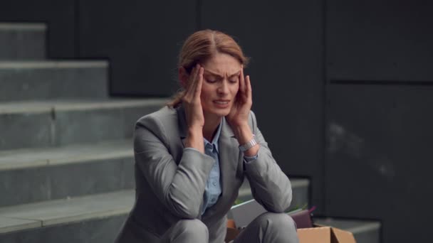 Переутомление и проблемы со здоровьем. Расстроенная работница средних лет, страдающая головной болью, отдыхающая на лестнице возле офисного здания, замедленная съемка, пустое пространство - Кадры, видео