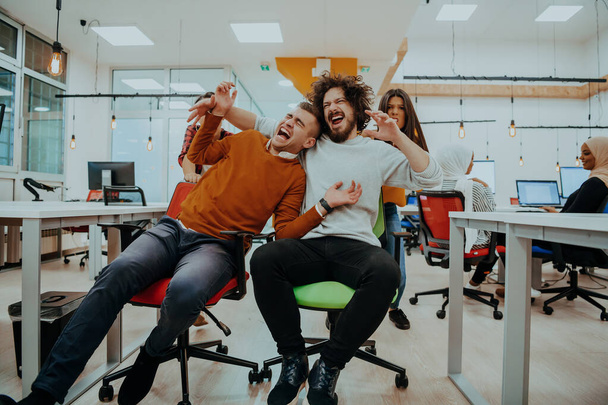 Team building and office fun. Young cheerful businesspeople in smart casual wear having fun while racing on office chairs and smiling - Foto, imagen