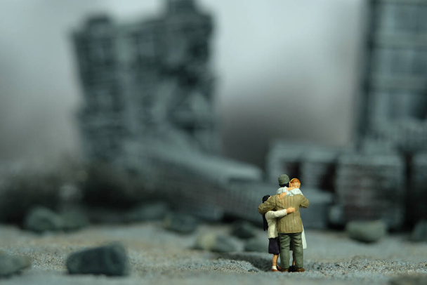 Miniatűr emberek játék figura fotózás. Családi összejövetel. Apa megöleli a feleségét és a lányát egy lerombolt város közepén. Képfotó - Fotó, kép