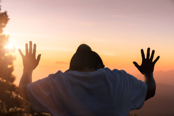 Faith of christian concept: Spiritual prayer hands over sunshine with blurred beautiful sunrise or sunset background. Christians who have believe, faith in God morning prayer. - Photo, Image
