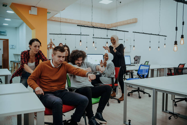 Team building and office fun. Young cheerful businesspeople in smart casual wear having fun while racing on office chairs and smiling - Fotografie, Obrázek