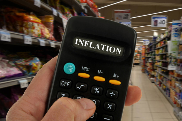Koncepcja inflacji z kalkulatorem w ręku z rozmytymi półkami supermarketów w tle - Zdjęcie, obraz