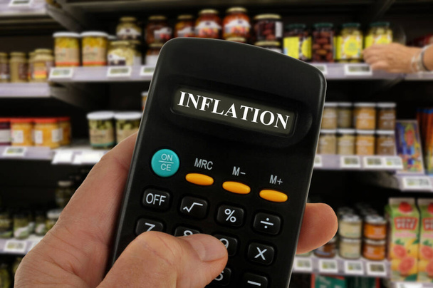 Koncepcja inflacji z kalkulatorem w ręku z rozmazaną półką supermarketu w tle - Zdjęcie, obraz