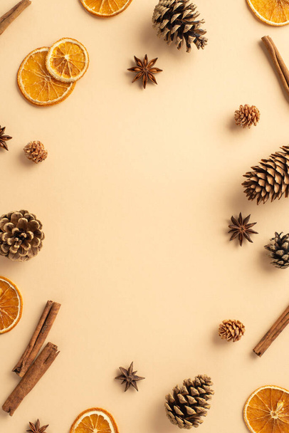 Top view vertical photo of dried orange slices pine cones anise and cinnamon sticks on isolated beige background with empty space in the middle - Photo, image