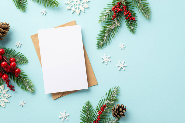 Winter holidays concept. Top view photo of craft paper envelope postcard fir branches pine cones mistletoe berries and snowflakes on isolated pastel blue background with copyspace - Foto, afbeelding