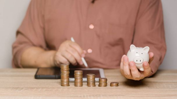 A man is calculating money to save and puts it in a piggy bank. Ideas for saving money for future home purchases and use in future after retirement. Family expenses. - Photo, Image