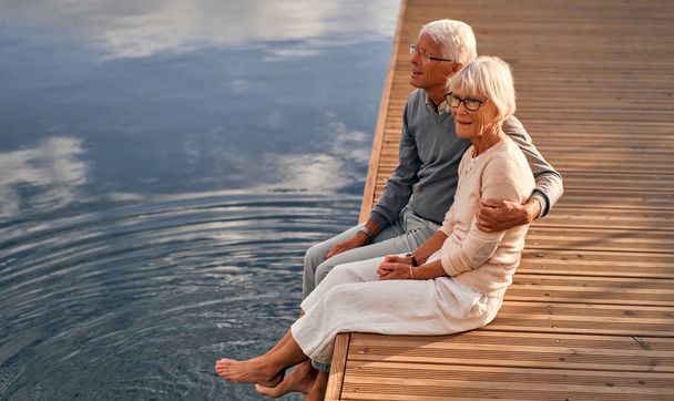 Пожилая, умная, седовласая влюбленная пара сидит на пирсе в морском порту, любоваясь морским пейзажем.. - Фото, изображение