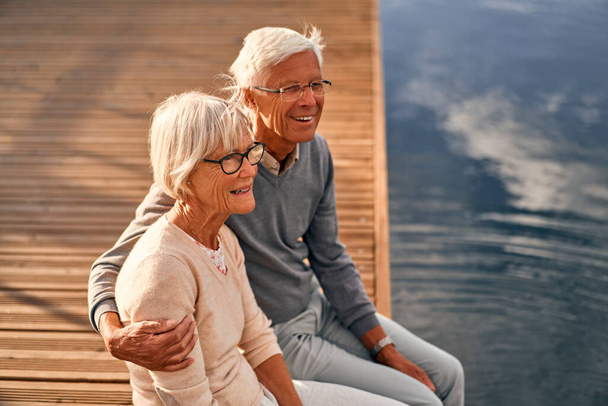 Egy idős, intelligens, ősz hajú szerelmespár ül a kikötőben egy kikötőben, romantikusan gyönyörködve a tengerben.. - Fotó, kép