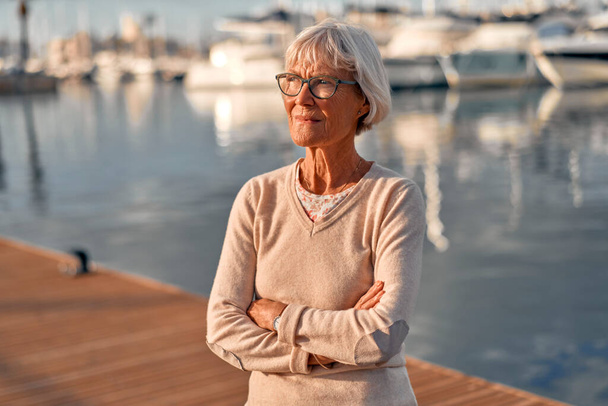 Starší inteligentní šedovlasá žena kráčející po molu v přístavu s luxusními jachtami a čluny, relaxující a obdivující mořskou pláň. - Fotografie, Obrázek