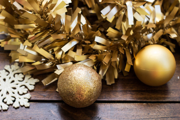 Golden Christmas balls with gold tinsel and snowflakes on wooden background - Valokuva, kuva