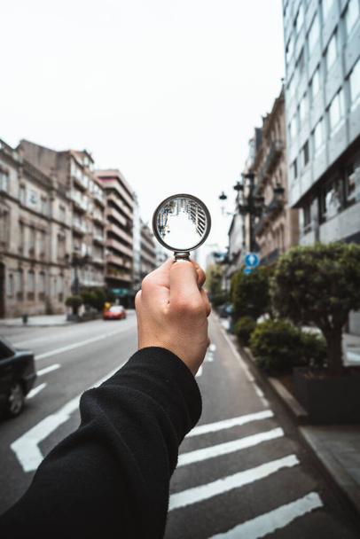 Man holding a magnifying glass towards a road in a city street - Photo, Image