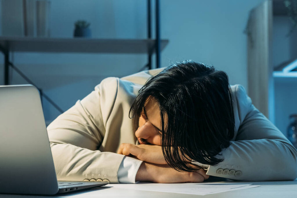 Work deadline. Sleeping man. Hard education. Office guy falling asleep laying on desk opened laptop dark light room interior. - Фото, изображение