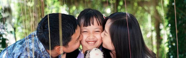 Parents embrassant leur fille souriante sur ses joues avec sourire et heureux - Photo, image