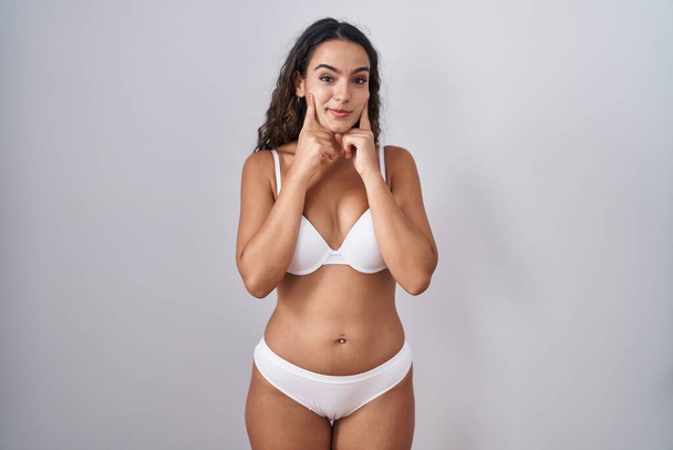 Young hispanic woman wearing white lingerie smiling with open mouth, fingers pointing and forcing cheerful smile  - Fotografie, Obrázek