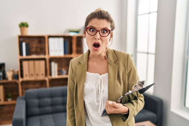 Mladá žena pracující v konzultační kanceláři v šokované tváři, skeptická a sarkastická, překvapená s otevřenými ústy  - Fotografie, Obrázek